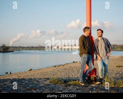 Smiling son and father leaning by pole while talking with each other at riverbank Stock Photo