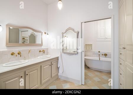 Interior of retro or classic style bathroom decorated in beige color with bath zone, two sinks and vintage mirrors Stock Photo