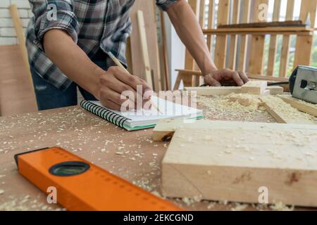 Carpenter working on wood craft at workshop to produce construction material or wooden furniture. The young Asian carpenter use professional tools for Stock Photo