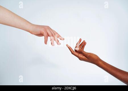 Friends stretching hands toward each other against white background Stock Photo