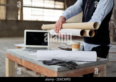 Male architect holding papers while standing at table in building Stock Photo