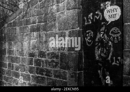 'Why Me' street art girl on door by brick wall on slopes of Calton Hill Edinburgh. Shot in dramatic black and white. Stock Photo