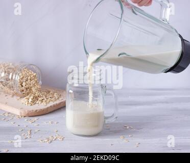 Vegetable oat milk is poured from a blender into a glass glass on a light background. Preparation of vegetable milk. Healthy drinks, vegetarianism. Si Stock Photo