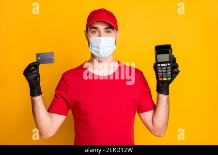 Portrait of healthy guy mailman wear mask holding in hands bank card terminal wireless transaction isolated on vivid yellow color background Stock Photo