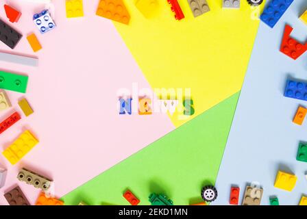 Words made of multi-colored wooden letters "news" on a multi-colored background, children's construction kit around. Top view. Stock Photo