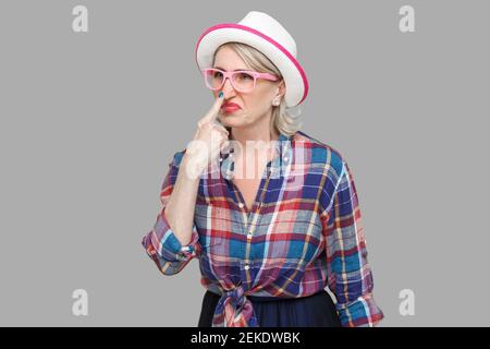 You are liar. Portrait of angry modern stylish mature woman in casual style with hat, eyeglasses standing looking and touching nose with lie gesture. Stock Photo