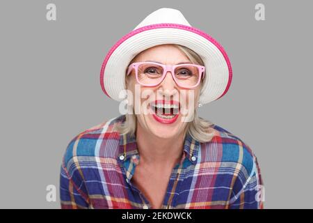 Portrait of happy modern stylish mature woman in casual style with hat and eyeglasses standing and looking at camera with surprised face and laughing. Stock Photo