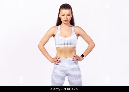 Self confident athletic woman in white sports tights and top looking at camera with confident motivated expression. Indoor studio shot isolated on gra Stock Photo