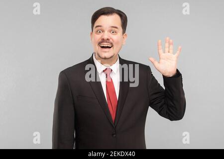 Well, hi! Positive boss showing hello sign, toothy smiling at camera, happy to see subordinates. indoor, isolated on gray background. handsome busines Stock Photo