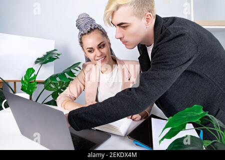Office work, business. Young attractive man helping his female colleague to deal with the project. He bent over her laptop, standing next to her as th Stock Photo