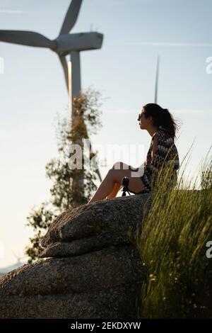 Caucasian woman on top of a boulder looking at wind turbines in Fafe, Portugal Stock Photo