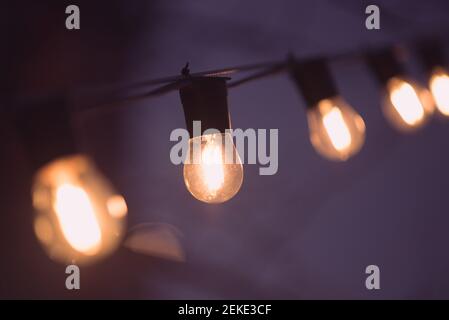 Garland of bulb lamps in darkness. Warm orange light in purple night. Stock Photo