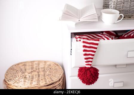 One white-red hat with a large red pompom hangs from an open drawer of a white chest of drawers. Stock Photo