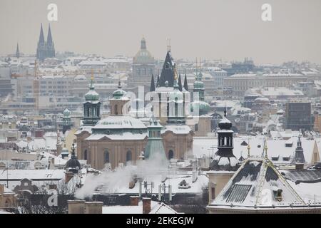 Snow covered historical centre of Prague with Saint Nicholas' Church (Kostel svatého Mikuláše) and the Old Town Hall (Staroměstská radnice) in Old Town Square and the National Museum (Národní muzeum) in Wenceslas Square (Václavské náměstí) pictured from the Hanavský Pavilon in Letná Park (Letenské sady) in Prague, Czech Republic. The church of Saint Ludmila (Kostel svaté Ludmily) is seen in the background at the left. The towers of Saint Gall's Church (Kostel svatého Havla) are seen next to the medieval tower of the Old Town Hall at the right. Stock Photo