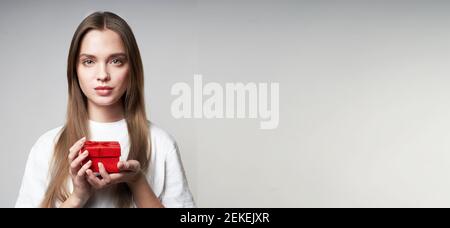 Beautiful young blonde woman on a gray background with a red small gift in hands. High quality banner Stock Photo