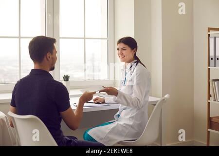 Positive woman medical worker sitting and giving paper prescriprion to man patient Stock Photo