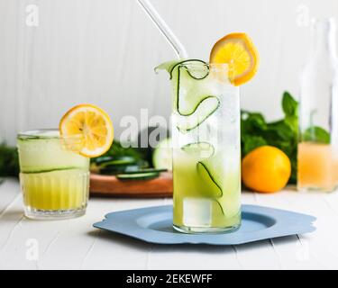 Light yellow-green cocktail and mocktail in a highball glass and rocks glass surrounded and garnished with cucumbers and lemon. Stock Photo