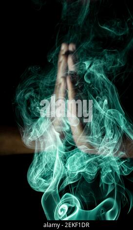 a out of focused human folded hands surrounded by green smoke in black background Stock Photo