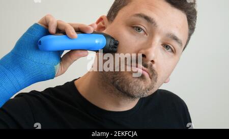 Man shaves his cheek with electric razor Stock Photo
