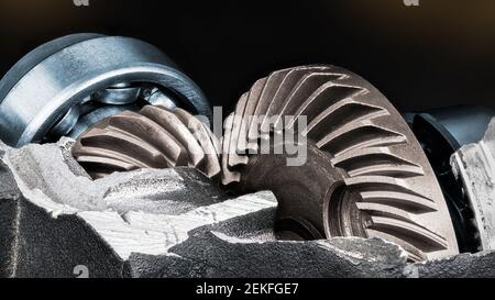 Metallic gear mechanism in detail of damaged engine case on black background. Interlocked steel cogged wheels and caged ball bearings in disc grinder. Stock Photo