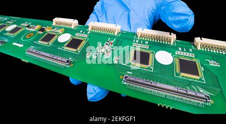 Long electronic printed circuit board on hand in blue glove. Surface-mount technology on green PCB detail. White connectors. Chips in protective gel. Stock Photo