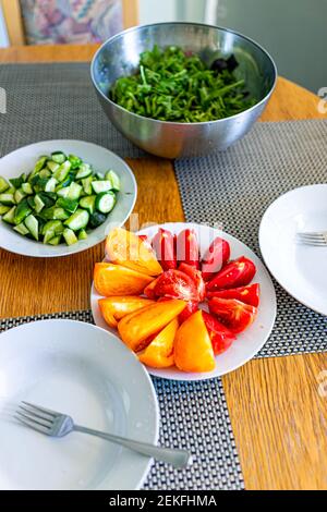 Fresh sliced ripe red orange yellow vibrant vivid tomatoes slices on plate closeup table as healthy snack or salad appetizer with cucumbers and arugul Stock Photo