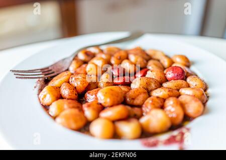 Closeup side view of fresh red wine sauce potato gluten free wheat gnocchi on white plate with lupine beans in Italian Italy restaurant with fork and Stock Photo