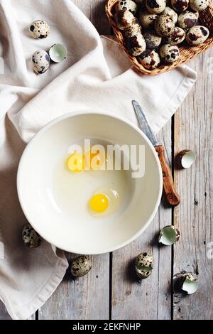 Broken quail eggs in a bowl on a wooden background. Stock Photo