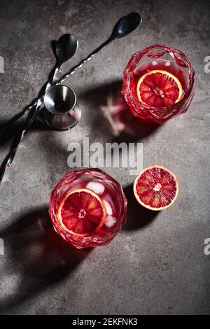 Negroni cocktail with ice cubes and blood orange on a dark gray stone background, top view.
