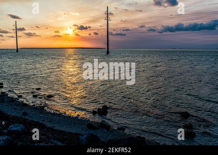 Sunset in Islamorada, Florida Keys with sky power lines pylons and water on gulf of Mexico or Atlantic Ocean horizon island rocks with view on coast s Stock Photo