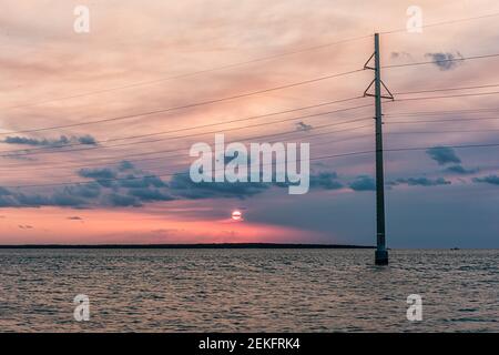 Sunset in Islamorada, Florida Keys with sky power lines pylon in water of Gulf of Mexico or Atlantic Ocean with island horizon by coast shore and sun Stock Photo