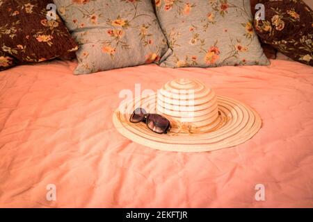 Elegant women's hat and sunglasses lying on a stylish bed. Warm light. The concept of a summer morning, vacation, pleasant relaxation Stock Photo