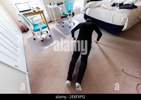 Young woman working out doing push ups workout exercise indoors at home in room bedroom with bed, chairs office tables Stock Photo