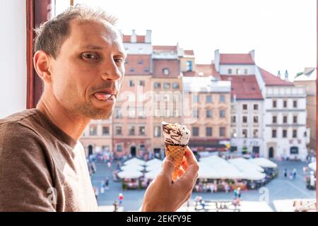 Man eating vanilla chocolate ice cream gelato cone with tongue out bokeh background of Warsaw old town market square in Europe city summer Stock Photo