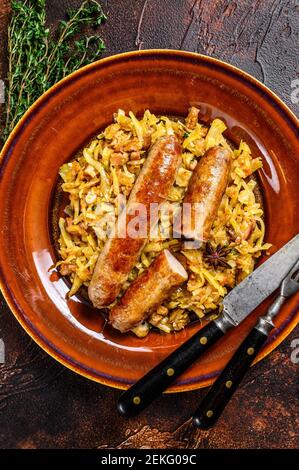 Bigos Stewed cabbage with mushrooms and meat sausages on a plate. Dark background. Top view Stock Photo