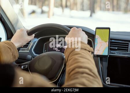 Hands of young contemporary active man in warm winterwear holding by steer while sitting in car and using map on screen of smartphone Stock Photo