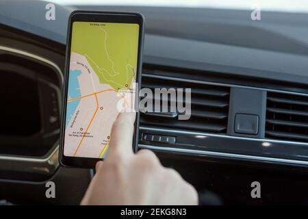 Hand of young man sitting in car and pointing at map on screen of smartphone while choosing place where he going to travel Stock Photo