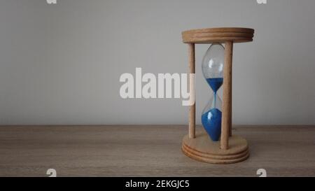 Pouring sand in an hourglass standing on an a wood desk. Pass of time and waste time concept. Catch the moment. Stock Photo