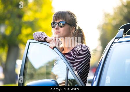 Young female driver resting near her car enjoying warm summer day. Travel and getaway concept. Stock Photo