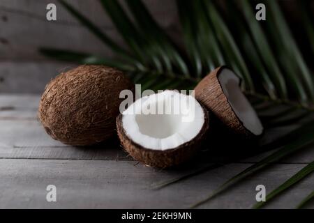 Broken coconuts on gray wooden background with palm leaf. White coconut pulp. High quality photo Stock Photo