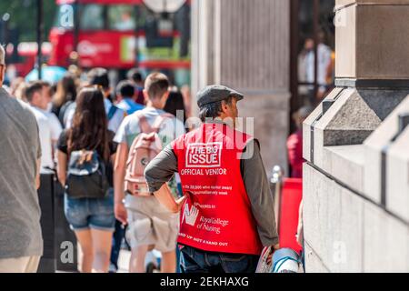 London, UK - June 25, 2018: People outside on sidewalk pavement in sunny summer with sign on man for big issue Stock Photo