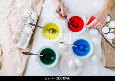 Close up hands Man dyeing Easter eggs with liquid food coloring. Flat lay. Stock Photo