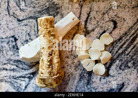 Horseradish in three different stages, raw, skinned, and sliced on a busy marble background.  Overhead angle.  Ready for use in recipes. Stock Photo