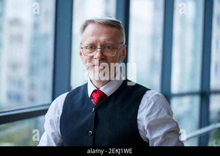 Smiling happy managing director thinks about his successful career development while stands in his office near the background of a window with copy sp Stock Photo