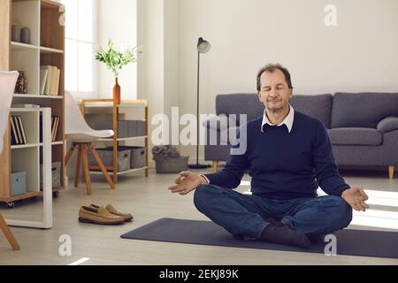 Happy relaxed mature man sitting on floor at home and meditating with eyes closed Stock Photo