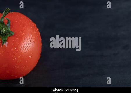 A fresh whole tomato with water droplets on a dark background Stock Photo
