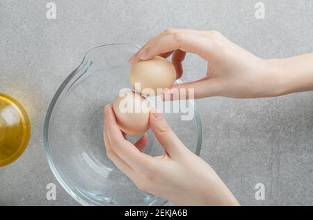 Female hands holding raw eggs on top of glass bowl Stock Photo