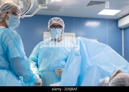 Young female assistant and professional male surgeon in workwear looking at screen of medical equipment during operation in clinics Stock Photo