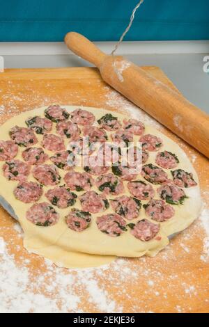 Cooking homemade dumplings on round form. Minced meat with spinach on thin rolled out dough. Close-up, selective focus. Stock Photo