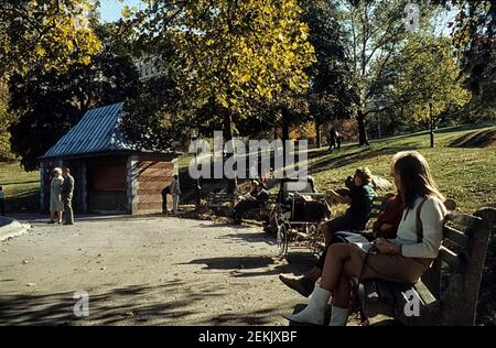 People sitting on wood-and-concrete NYC benches enjoying the autumn sun. Central Park, Manhattan, New York City, USA, 1965 Stock Photo